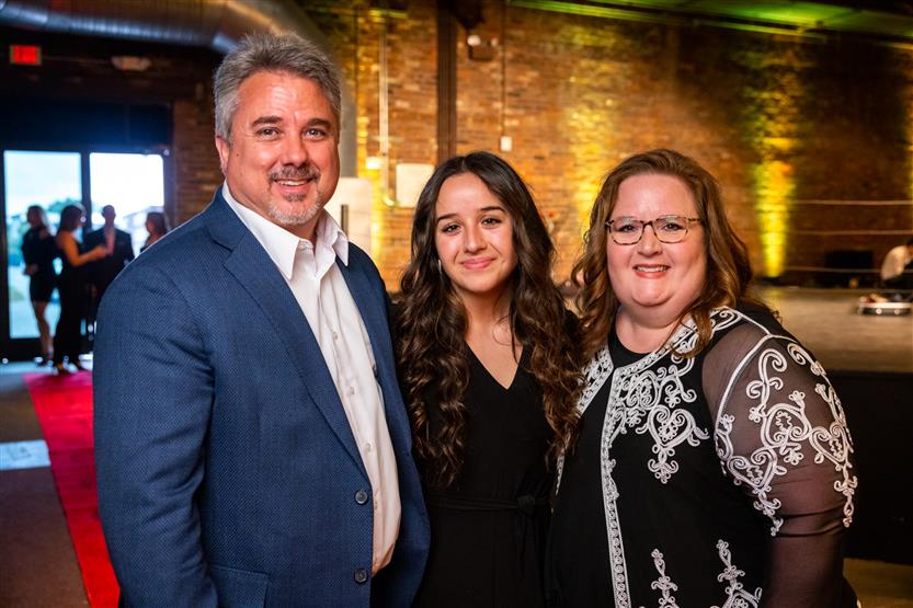 A man wearing a blue blazer, a woman wearing a black shirt and a woman wearing a black and white top smile